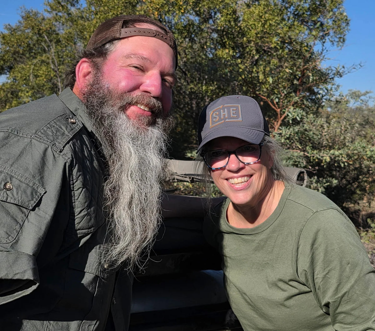 Two people outdoors with trees and a clear sky in the background